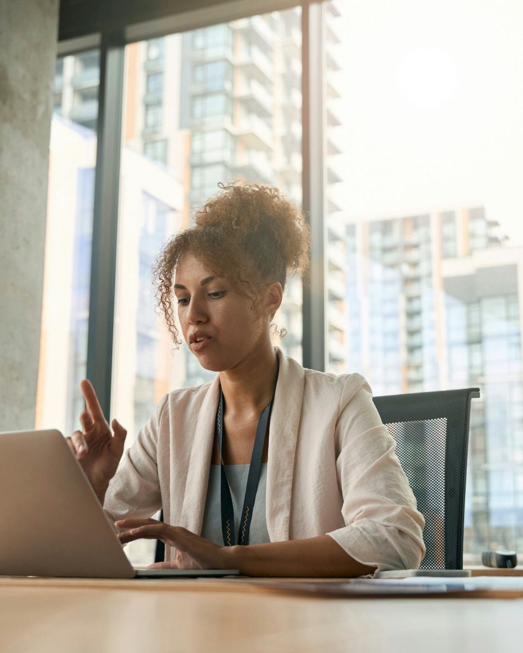 A professional working on a laptop at a table by a tall window
